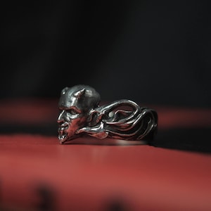 May include: A silver ring featuring a detailed design of a demon's head with horns and a flowing mane.