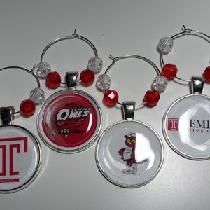 May include: A collection of wine charms featuring the Temple University Owls logo and imagery. Each charm has a silver hoop, a pendant with a logo, and red and clear beads. The charms are designed for wine glasses.