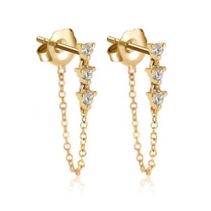 May include: A pair of gold earrings with a delicate chain and three small clear stones.