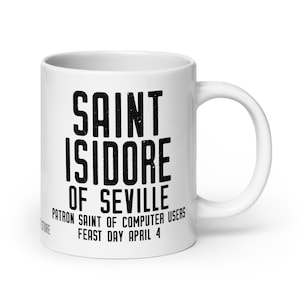 May include: White ceramic mug with the text "SAINT ISIDORE OF SEVILLE, PATRON SAINT OF COMPUTER USERS, FEAST DAY APRIL 4" in black. The mug has a curved handle and is designed for hot beverages.