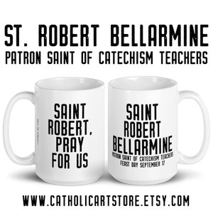 May include: White ceramic coffee mug with black text that reads "Saint Robert, Pray for Us" on one side and "Saint Robert Bellarmine Patron Saint of Catechism Teachers Feast Day September 17" on the other side.