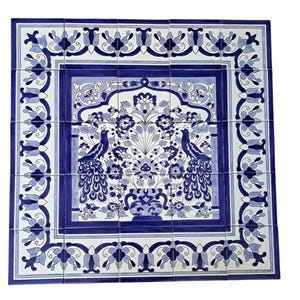 Könnte beinhalten: Ein quadratisches Wandbild aus fünfundzwanzig Keramikfliesen mit blau-weißem Muster. Das Design zeigt zwei Pfauen, die eine zentrale Blumenvase flankieren, umgeben von einer dekorativen Bordüre aus stilisierten Blumen und Ranken.