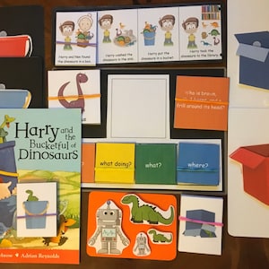 May include: A children's book titled "Harry and the Bucketful of Dinosaurs" with illustrations of a boy carrying a bucket full of dinosaurs. The book is accompanied by a set of educational cards with images and text related to the story.
