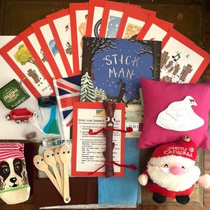 May include: A Stick Man sensory pack for children, featuring a book, sensory items and a plush Santa Claus toy. The pack includes a red stick, a white swan pillow, a blue and white sensory bottle and a set of wooden spoons with googly eyes. The book is titled "Stick Man" and features a red, white and blue Union Jack flag.