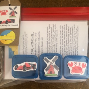 Puede incluir: Una bolsa de plástico transparente contiene un juego de juguetes educativos para niños. El juego incluye tres recipientes cuadrados azules con pegatinas de un coche de carreras rojo, un molino de viento rojo y un cangrejo rosa. Una etiqueta muestra las mismas imágenes.