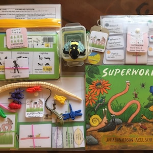 May include: A Superworm themed educational game set with a book, cards, and plastic figurines. The book is titled "Superworm" by Julia Donaldson and Axel Scheffler. The cards feature images of animals and insects, including a bee, a frog, a snail, and a worm. The plastic figurines include a bee, a frog, a snail, a worm, and a spider.