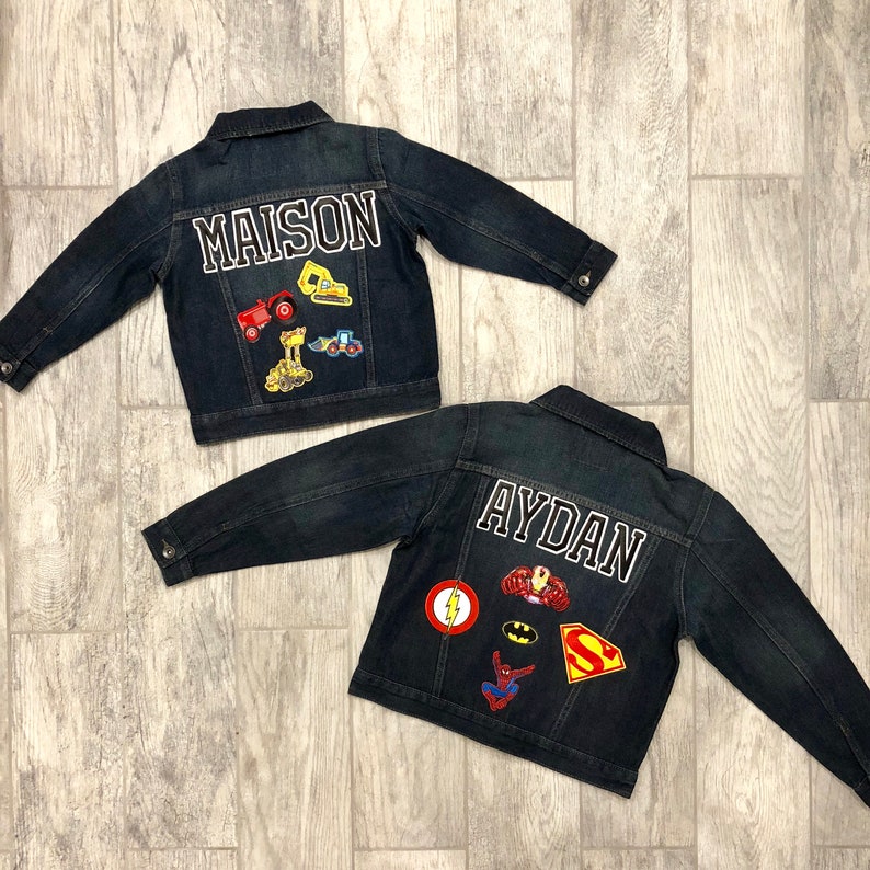 May include: Two denim jackets with personalised patches. One jacket has the name "MAISON" with construction vehicle patches. The other jacket has the name "AYDAN" with superhero patches.
