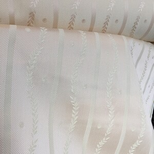 May include: Cream-colored fabric roll with a repeating pattern of vertical stripes, dotted circles, and leaf-like designs. The fabric has a subtle texture and a soft, neutral color palette, suitable for upholstery or drapery.