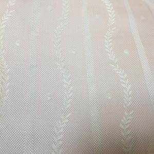 May include: Close-up of a light pink fabric with a textured, dotted pattern. Vertical stripes alternate with delicate, off-white leaf designs. The fabric has a subtle sheen, suggesting a soft, drapable material.