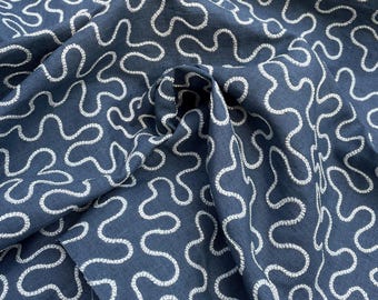 May include: Close-up of a navy blue fabric with a white, wavy, embroidered pattern. The fabric is folded, showing the texture and design. The pattern is a continuous, flowing line.