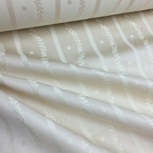 May include: Cream-colored fabric with a repeating pattern of vertical stripes, dotted accents, and stylized leaf designs. The fabric is folded, showing the texture and sheen of the material. The overall aesthetic is elegant and suitable for home decor.