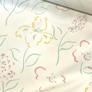 Puede incluir: Papel pintado floral crema con un patrón repetido de flores y hojas estilizadas. El diseño presenta elementos amarillos, rosas y verdes sobre un fondo crema. El papel pintado está enrollado, mostrando el patrón.