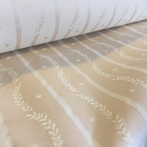 May include: A roll of fabric with a repeating pattern of vertical stripes in cream and beige. White leaf and dot details are interspersed between the stripes. The fabric has a woven texture.