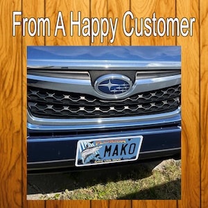 Puede incluir: Un coche Subaru plateado con una parrilla negra y una matr&iacute;cula de Florida que dice "MAKO" con un gr&aacute;fico de pescado. La matr&iacute;cula tiene el texto "Save Our Sharks".