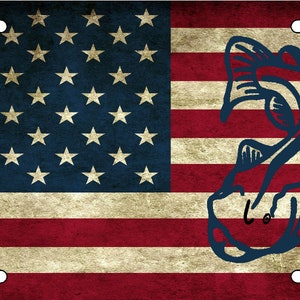 May include: A vintage-style American flag with a blue silhouette of a fish jumping out of the water. The flag has a distressed look, with faded colors and a textured surface.