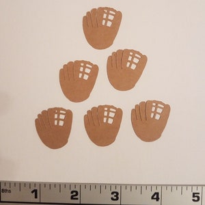 May include: Six brown paper cutouts of baseball mitts. The mitts are arranged in a triangular shape. A ruler is visible at the bottom of the image.