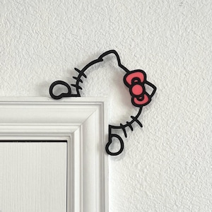 Puede incluir: Esquema en blanco y negro de Hello Kitty asomándose por un marco de puerta blanco. El lazo rojo característico de Hello Kitty es visible.