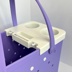 May include: A purple tote bag with a white tray that has two cup holders and a small compartment. The bag has a handle and white circular accents. The tray is designed to sit on the bag's rim.