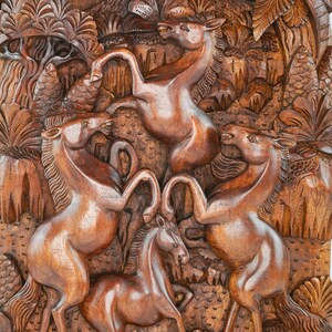 May include: A wooden wall carving depicting four horses in a jungle setting. The horses are carved in a realistic style and are shown in various poses. The carving is made of dark brown wood and has a natural finish.