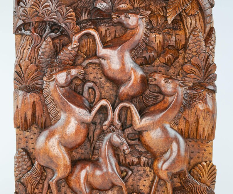 May include: A wooden wall carving depicting four horses in a jungle setting. The horses are carved in a realistic style and are shown in various poses. The carving is made of dark brown wood and has a natural finish.