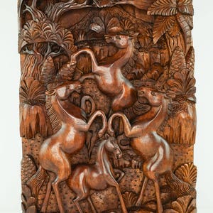 May include: A wooden wall sculpture depicting four horses in a jungle setting. The horses are carved in a realistic style and are shown in a dynamic pose. The sculpture is made of dark brown wood and has a natural finish.
