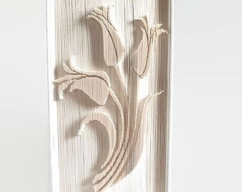 May include: A white book art sculpture of a bouquet of flowers. The flowers are made from folded pages of the book and are arranged in a vase shape.