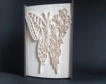 May include: A white paper butterfly with floral details is folded into a book shape. The book is bound in black fabric.