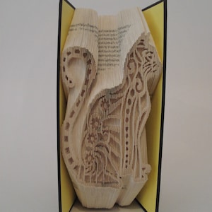 Op de afbeelding: Een boekkunst sculptuur van een kat, gevouwen uit de pagina's van een boek. Het beeld staat op een gele en zwarte boekomslag.
