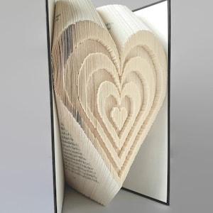 Op de afbeelding: Een boek met pagina's die zijn gevouwen in de vorm van een hart. Het boek is open en het hart is zichtbaar vanaf de zijkant. Het boek is gebonden in zwart.