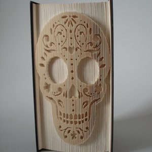 Puede incluir: Una escultura de arte de libro de una calavera de azúcar, un símbolo tradicional mexicano del Día de Muertos, hecha doblando las páginas de un libro.