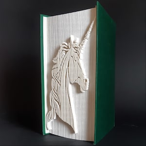 May include: A white paper book with a green cover, folded into the shape of a unicorn. The unicorn is facing the right side of the image.