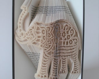 May include: A book art sculpture of an elephant made by folding the pages of a book. The elephant is white and has intricate details.