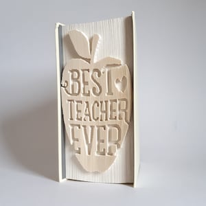 May include: A white book with a folded paper design of a red apple with the words "Best Teacher Ever" inside.