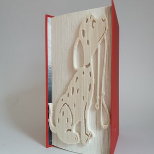 Könnte beinhalten: Ein weißes Buch mit einem Dalmatiner, der in die Seiten gefaltet ist. Das Buch steht aufrecht und hat einen roten Einband.
