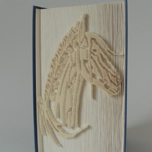 Peut inclure: Un livre blanc avec un motif de cheval créé en pliant les pages. Le livre a une reliure bleue.