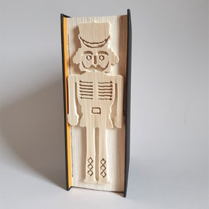 May include: A book with a nutcracker design carved into the spine. The book is black with a yellow spine.