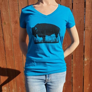 May include: A turquoise blue v-neck t-shirt with a black silhouette of a bison printed on the front.