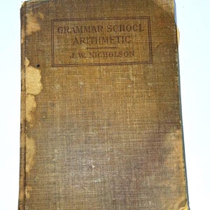 May include: A vintage book titled "Grammar School Arithmetic" by J.W. Nicholson. The cover is a faded brown with visible wear and tear, including stains and discoloration. The title is in a rectangular box.