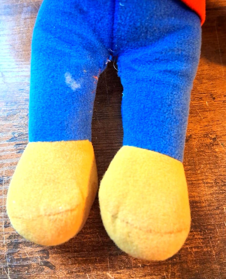 K&ouml;nnte beinhalten: Nahaufnahme der Beine eines Pl&uuml;schtiers. Die Beine sind blau mit gelben F&uuml;&szlig;en. Die Beine des Spielzeugs bestehen aus einem weichen, flauschigen Material. Auf dem linken Bein befindet sich ein Fleck.