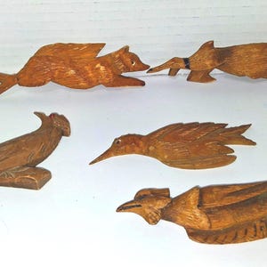 May include: Five hand-carved wooden animal figurines. The collection includes a bear, a duck, a bird on a branch, a bird in flight, and a bird with a crest. Each piece is crafted from light brown wood.