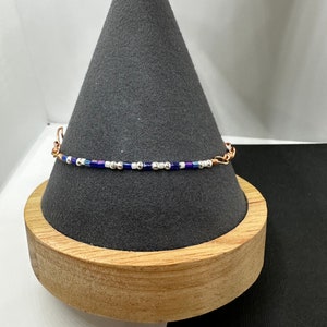 May include: A delicate bracelet made with small blue, white, and silver beads on a copper wire base.