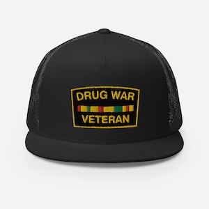 May include: Black trucker hat with a yellow embroidered patch that says "Drug War Veteran" and a yellow, red, and green ribbon.