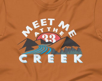 May include: A brown t-shirt with a graphic design of a mountain range with a river and the text "Meet Me At The 33 Creek".