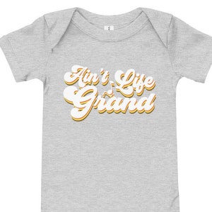 May include: A grey baby onesie with the text "Ain't Life Grand" in a retro font with yellow and orange accents.