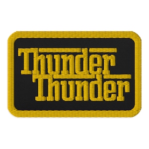 May include: Embroidered patch with the word "Thunder" stacked on top of itself in a bold, yellow, block letter font. The text is on a black background, framed by a yellow border. The patch has a rectangular shape.