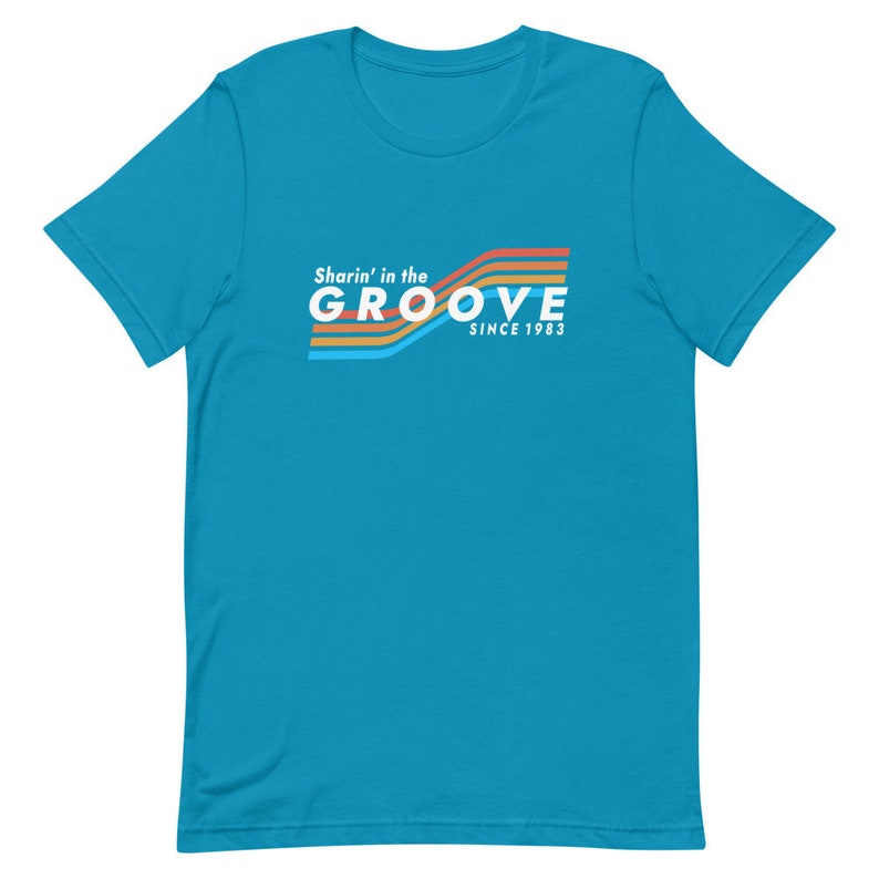 May include: A turquoise blue t-shirt with a retro-style graphic design. The graphic features a rainbow of colors and the text "Sharin' in the GROOVE since 1983".