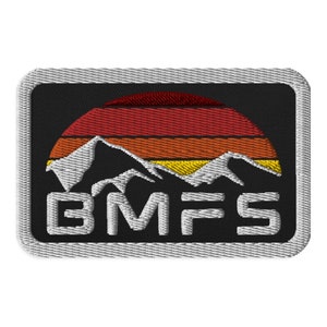 May include: A black embroidered patch with a white mountain range silhouette in front of a red, orange, and yellow sunset. The text "BMFS" is below the mountains in white.