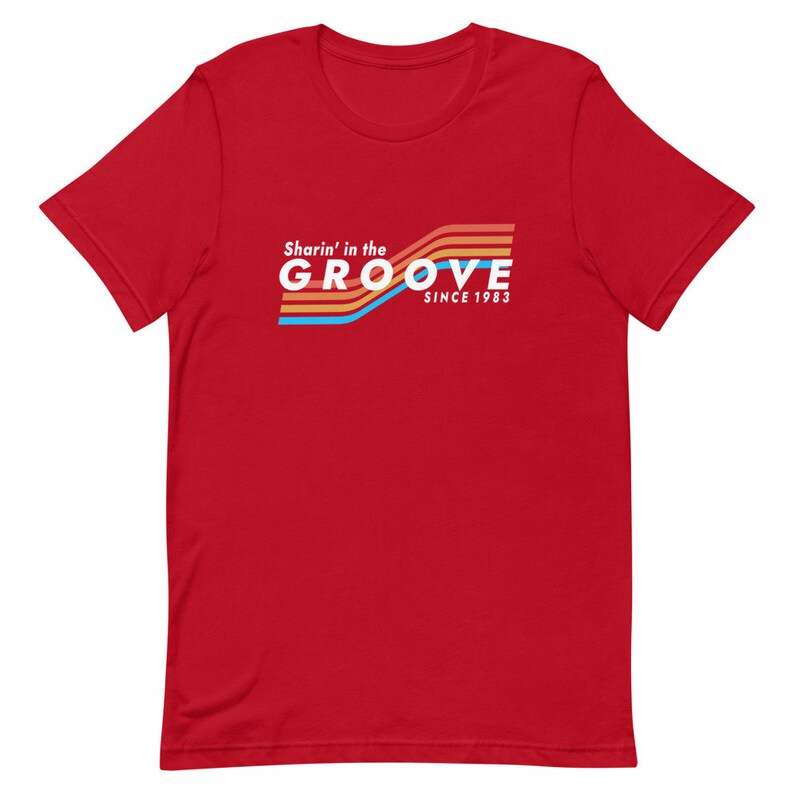 May include: Red t-shirt with a retro-style graphic that says "Sharin' in the GROOVE since 1983". The graphic features colorful stripes.