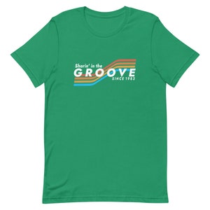 May include: Green short-sleeved t-shirt with a retro-style graphic that says "Sharin' in the GROOVE since 1983" in white text with colorful stripes.