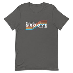 May include: A dark gray t-shirt with a retro-style graphic that says "Sharin' in the GROOVE since 1983" in white text with colorful stripes.